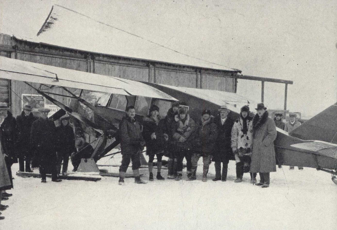 Group of men standing in front of plane on skis