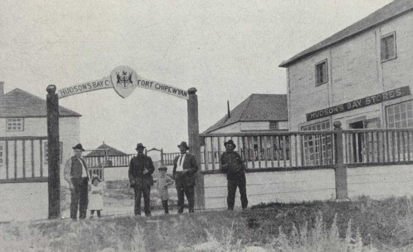 Group of men stand before fur-trading post