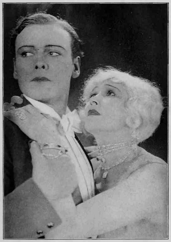 Bleached blonde woman clings to man and looks wistfully up at him