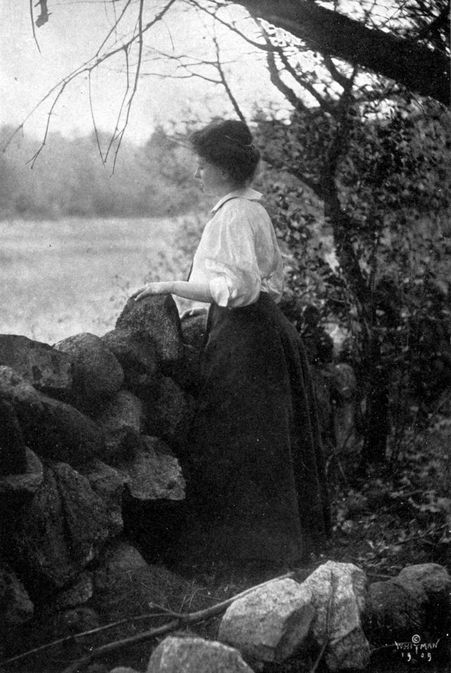 Helen is wearing a long skirt and standing next to a stone wall