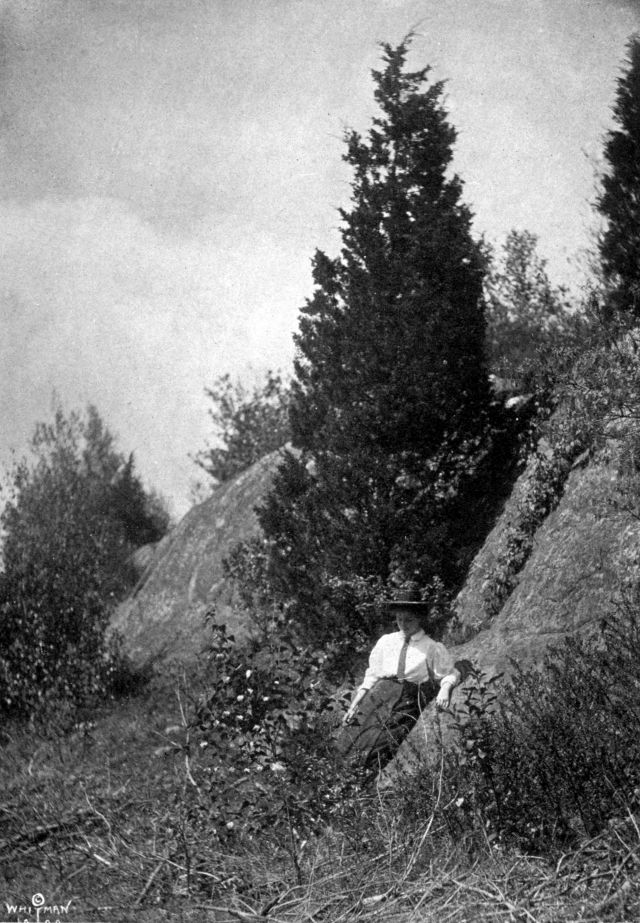 Helen wearing a hat is leaning against a large rock