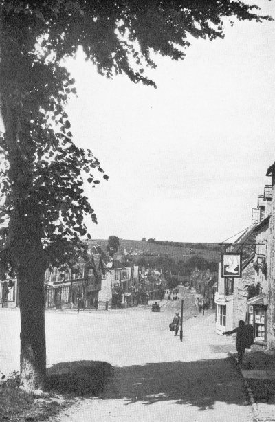 looking downhill on a 4-lane wide village street with hills in the background
