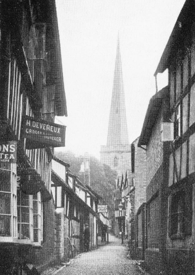 a small walking alley between two-story houses with church spire at the end of the walkway