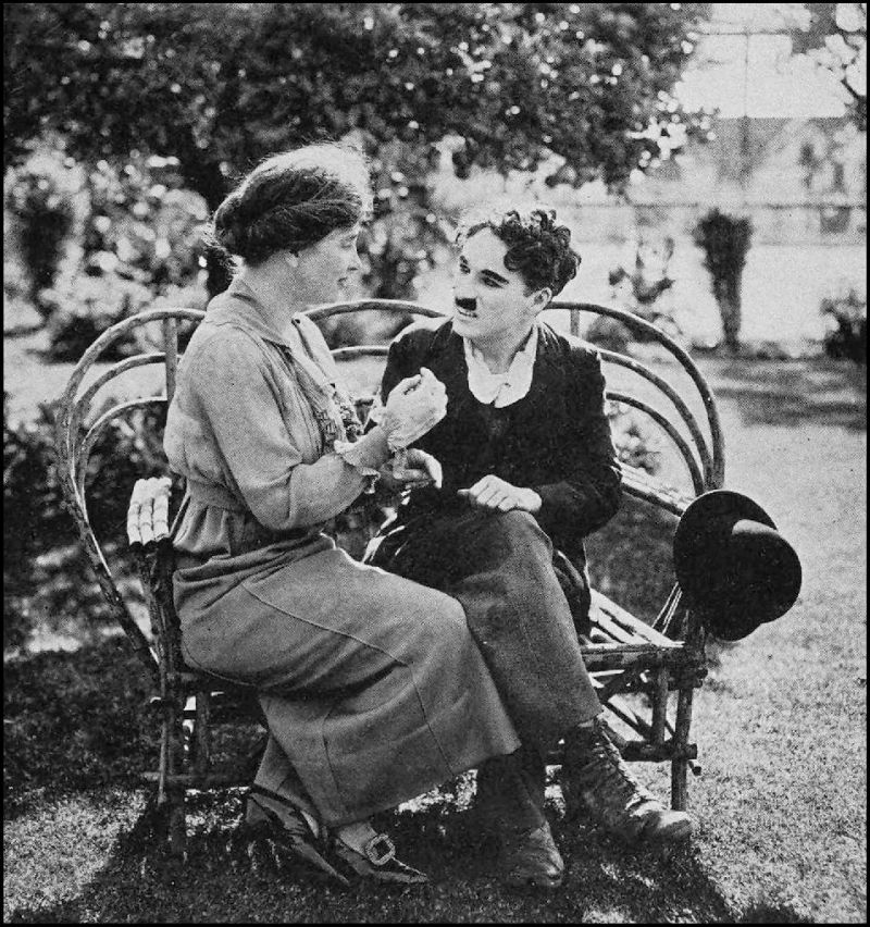 A man and a woman are seated on a wooden bench. The woman is gesturing with her hands as the man watches her.