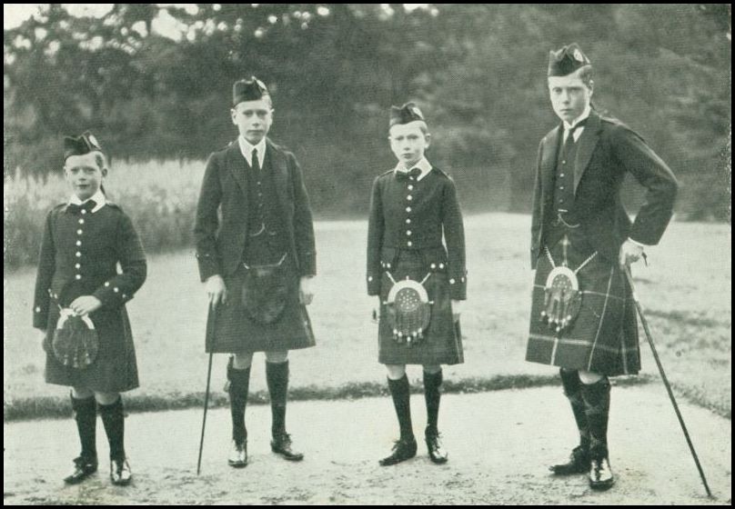 Four boys, all wearing kilts, are standin in an outdoor setting. Two of the older boys have canes.