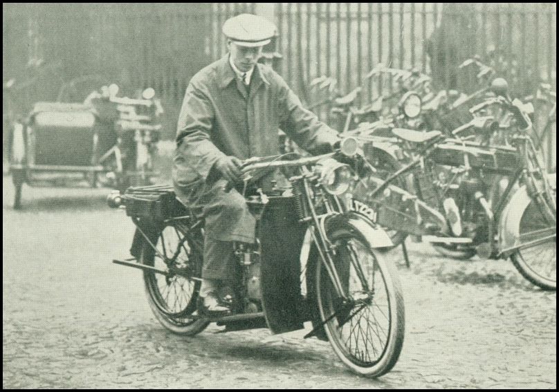 A man is riding a motorcycle on the street. There are other motorcycles and bicycles in the background.