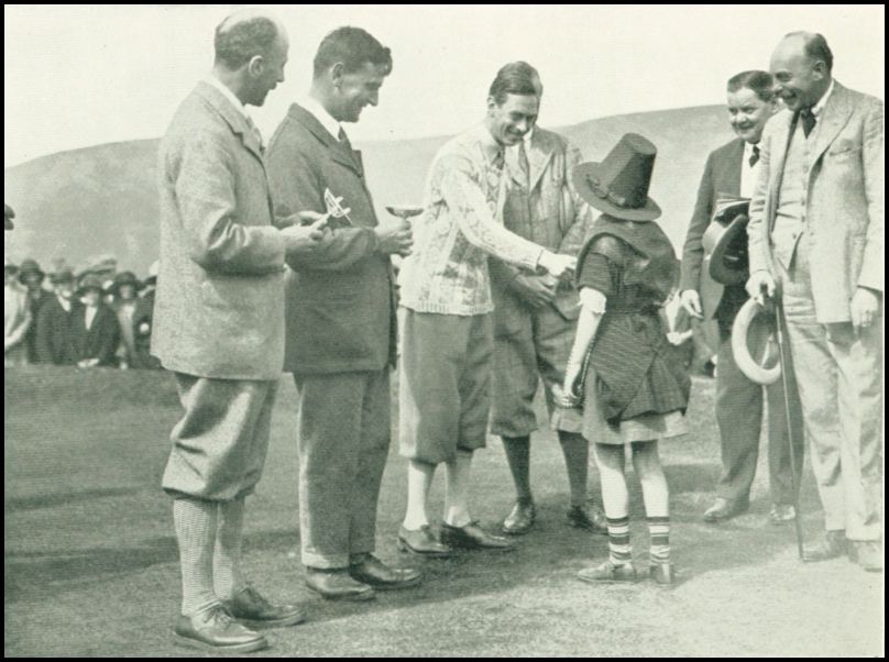 A group of men are standing around a young girl who is shaking the hand of one of the men.