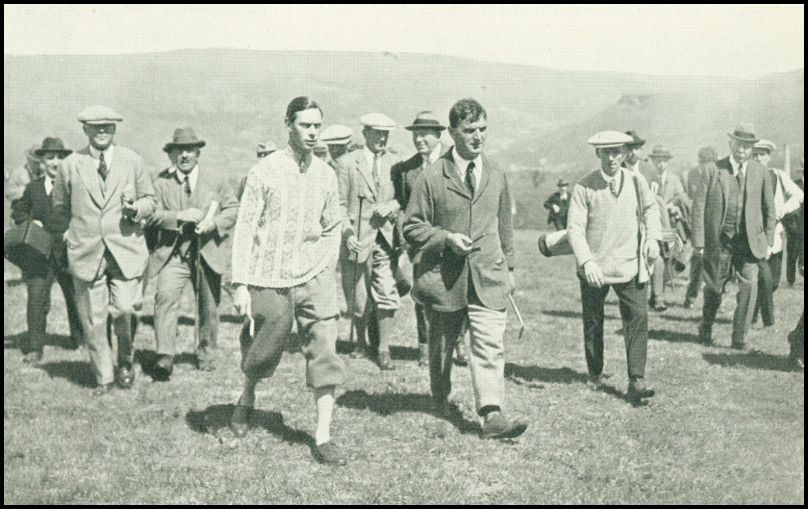 Two men playing golf are followed by another group men who appear to be watching the game.