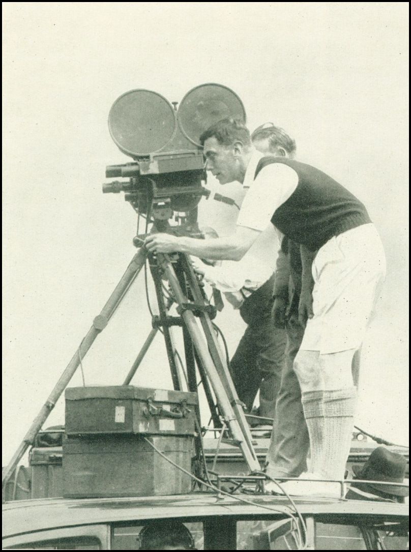 A man is looking through the viewfinder of an old-fashioned movie camera.