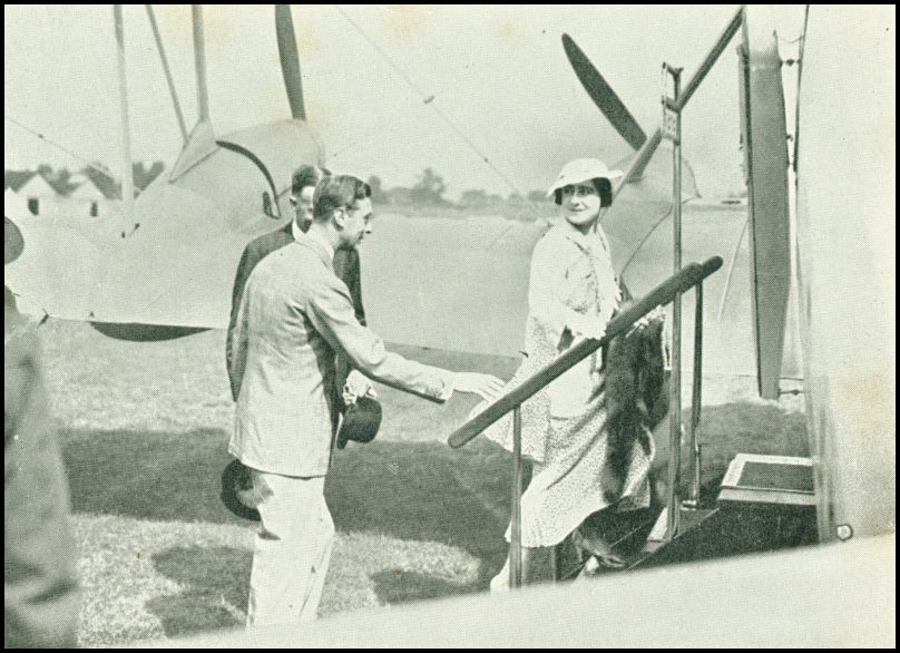 A woman is walking up the steps into an airplane and is looking back at a man that is following behind. There is another airplane in the background.