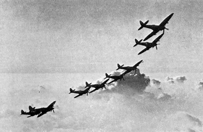 The photo shows eight planes flying in a linear formation with clouds in the distance.
