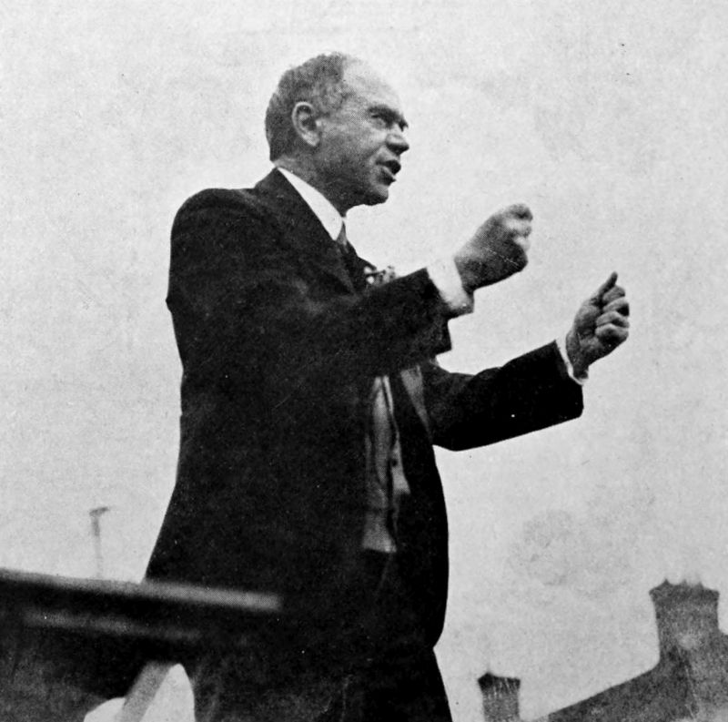 The photo shows a man standing in an outdoor setting. The man has his fisted hands upraised.
