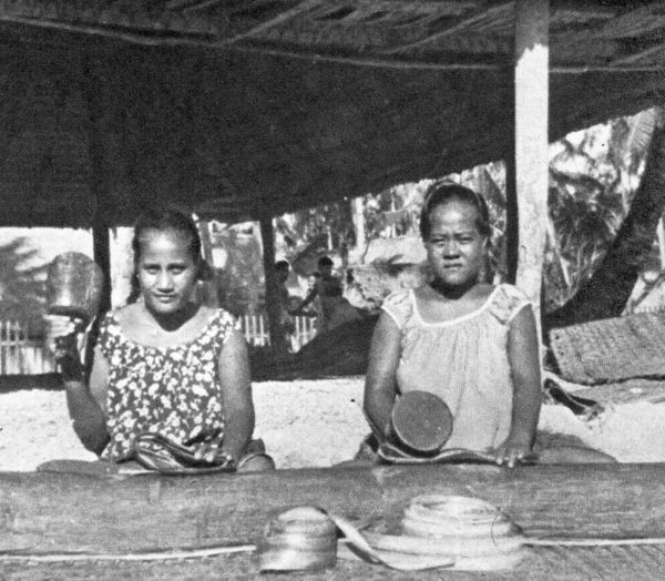 two women sitting and pounding pandanus leaves with round wood mallets
