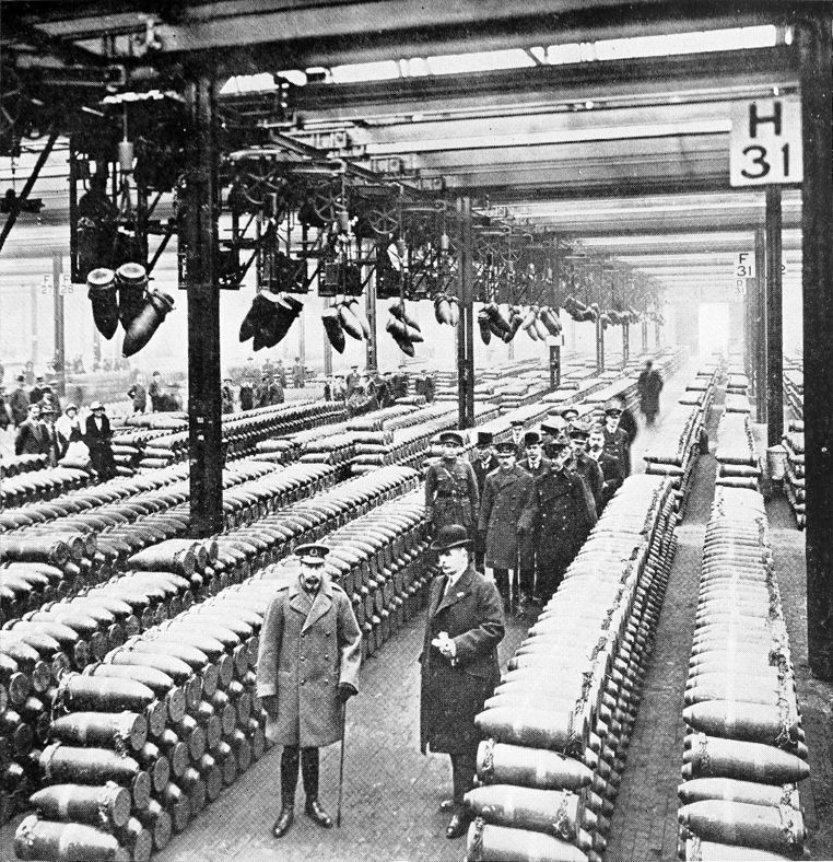 men standing among rows of artillery shells