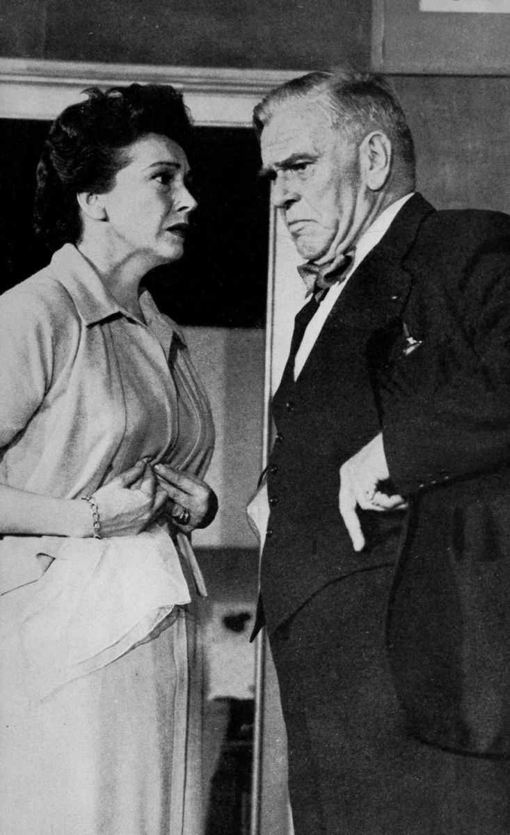 Christine with a worried look and hands on her stomach facing an elderly man in a suit who has a deep frown