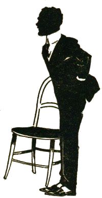sideview of suited man standing next to chair with hand in pocket