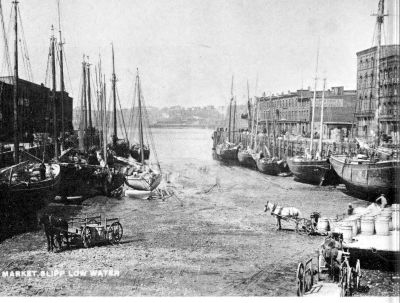ships sitting in mud of harbour, horse carts loaded with barrels
