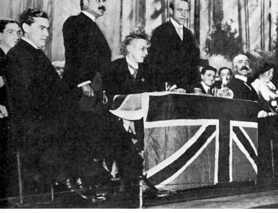 4 men sitting on a stage with Union Jack trimming; two men standing