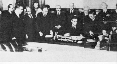 12 men standing around a seated man signing papers