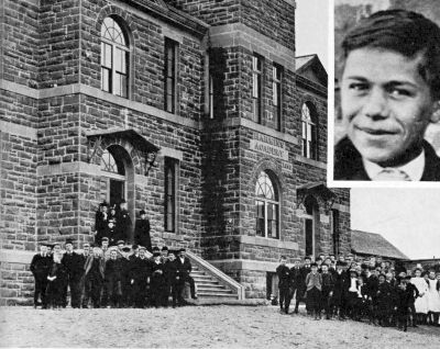 2 story stone schoolhouse with boys and staff posing in front