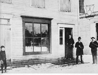 wooden storefront with 3 men and small boy standing in front