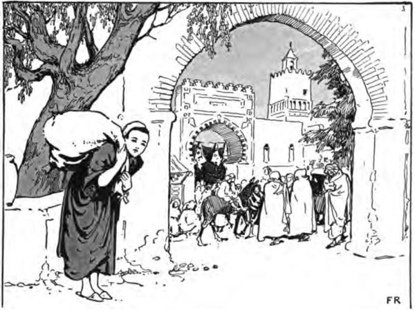 a boy carrying a sack at the gateway to an Arabic town