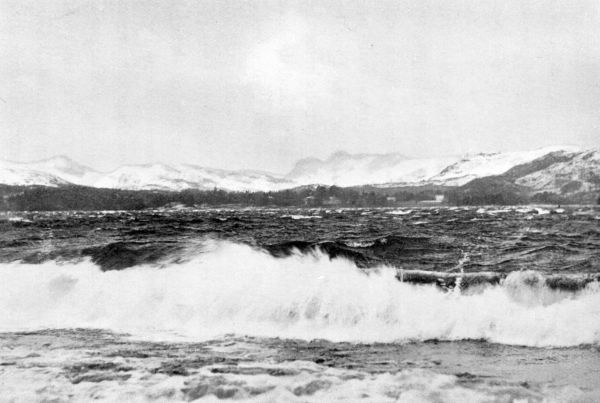 choppy waves on water with snow-covered hills behind