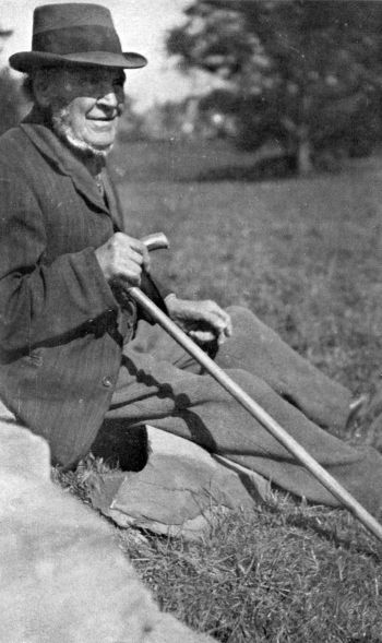 man wearing a hat sitting on the grass with a wood cane