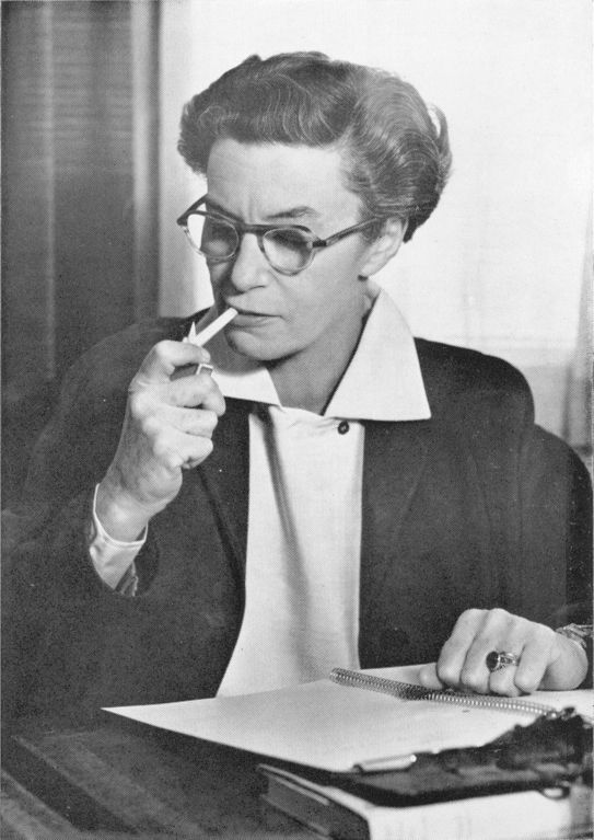 Author at writing desk, lighting a cigarette.