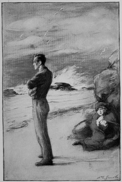 Varge in civilian clothes standing on stormy beach with woman crouched next to rock