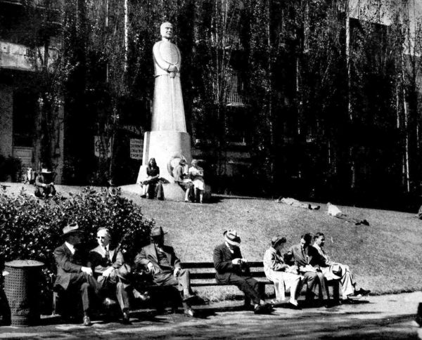 statue in front of building with men and women sitting in benches in front