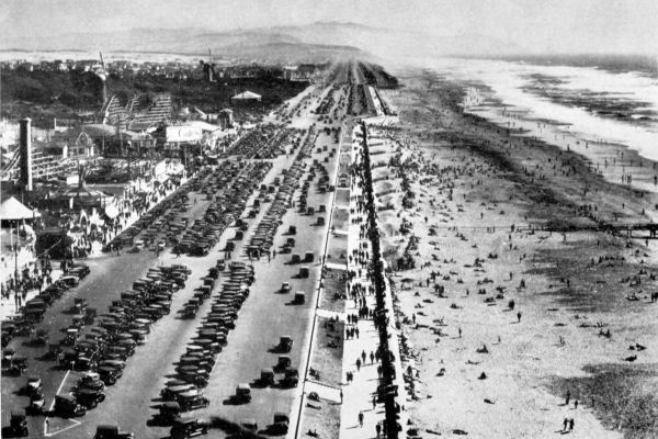 looking down from Cliff House onto Ocean Beach bathers and rows of parked cars with amusement park across the street