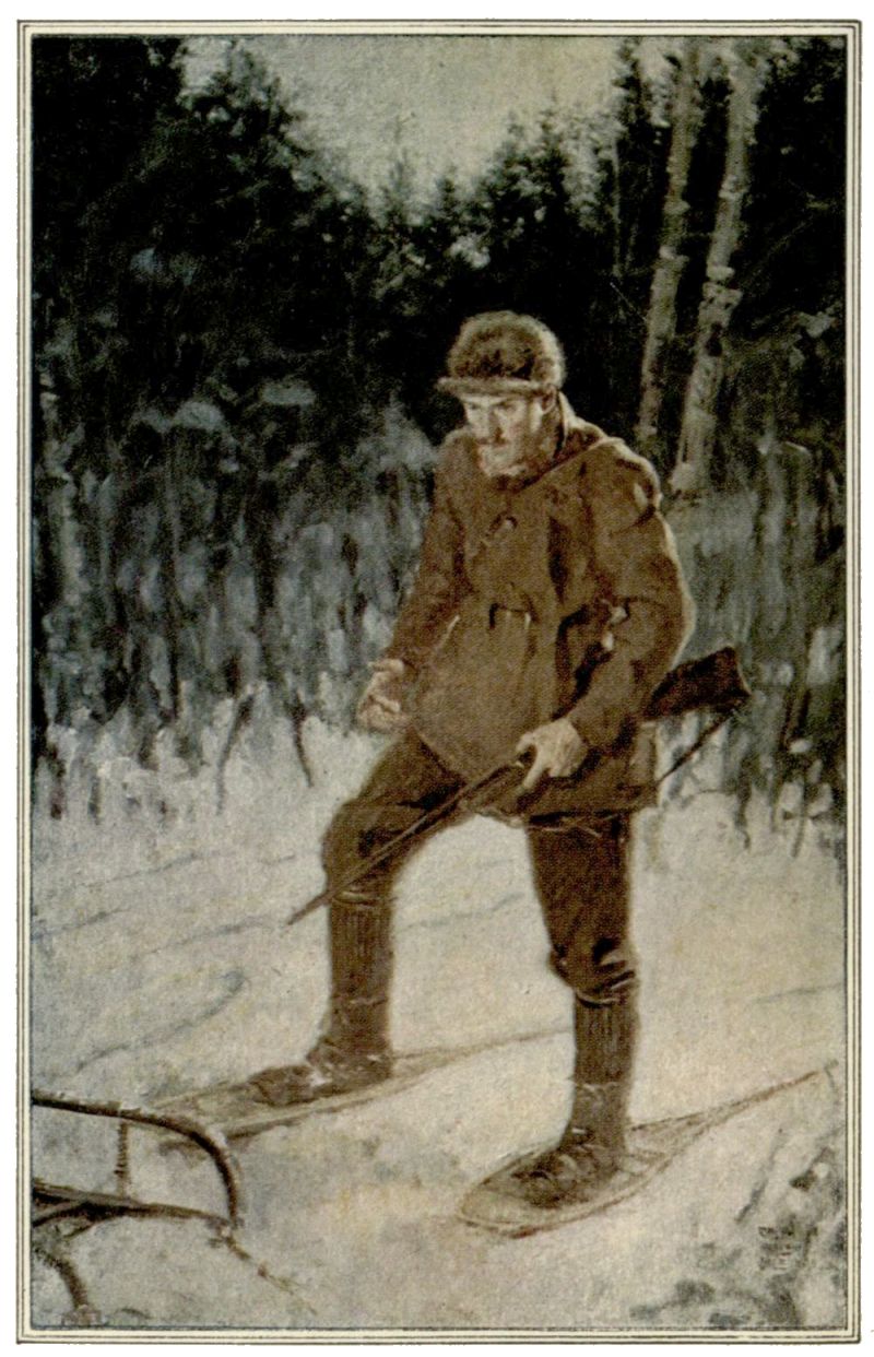 In a snow covered forest scene, a man dressed in winter clothing, carrying a rifle and wearing snowshoes, is standing and looking down towards an overturned sled.