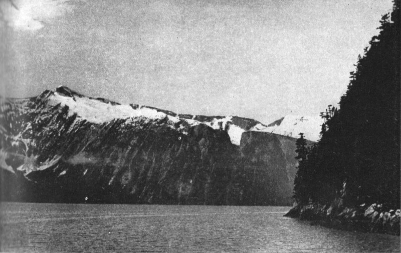Photo of towering mountains rising from the waterline.