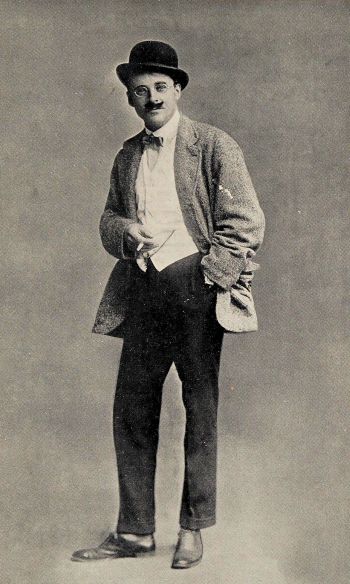 author wearing bowler hat, moustache and glasses and wearing man’s coat and trousers