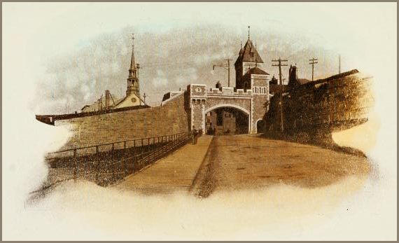 Image shows a fortified stone gate with tall spired towers rising above an arched entrance, set along a wide roadway bordered by heavy masonry walls and a distant church steeple.