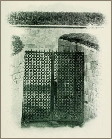 Image shows a heavy iron gate set into a stone passageway with spiked latticework on the tops of the gate.