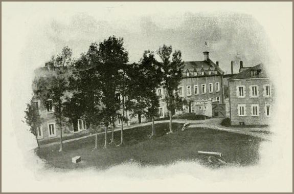 Image of a large brick institutional building with a central cupola, surrounded by a grassy courtyard and trees.
