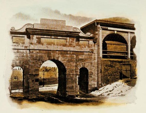 Image shows a massive, classically styled stone gateway with arched openings and upper windows rising from a snowy landscape.